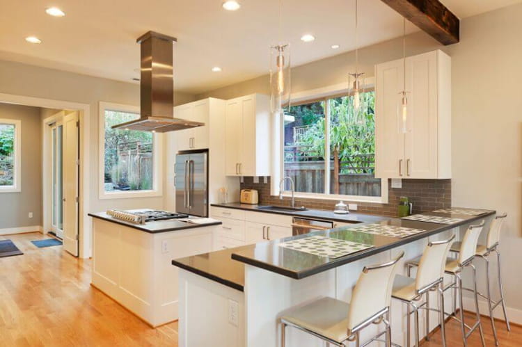 A modern kitchen with white cabinets and black granite countertops. The cabinets have silver handles and the walls are painted a light gray color. The kitchen has stainless steel appliances and a small island with a black countertop.
